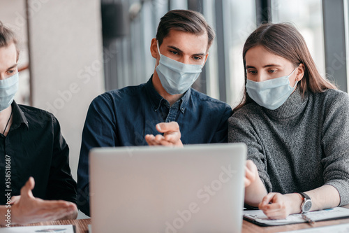 business team in protective masks sitting at the Desk.