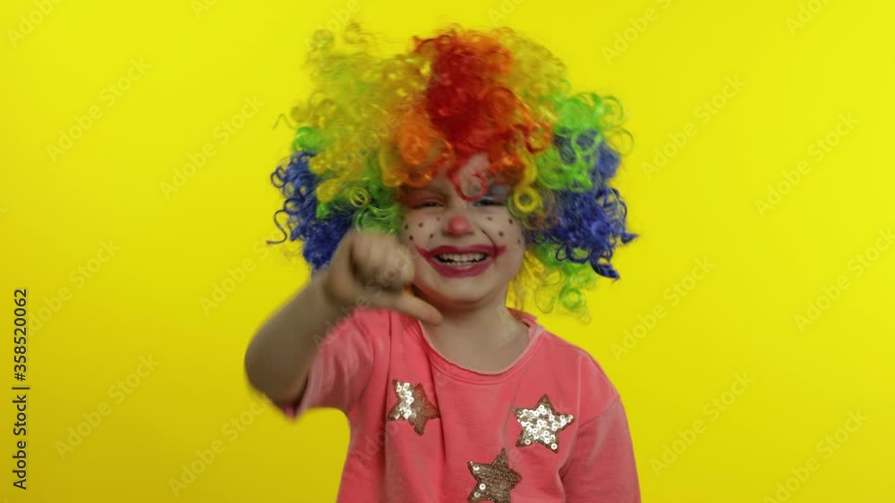 Little Child girl clown in rainbow wig making silly faces. Having fun, smiling. Thumb up. Halloween Little Child girl clown in rainbow wig making silly faces. Having fun, smiling. Thumb up. Halloween
