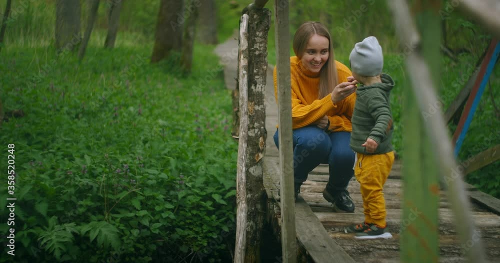 On the forest bridge, mother and son throw stones into the stream. Mother and boy spend time together on walks in the Park On the forest bridge, mother and son throw stones into the stream. Mother and boy spend time together on walks in the Park