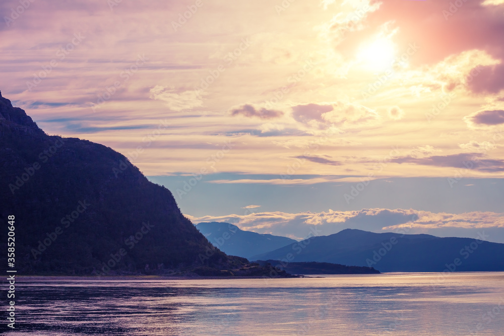 Mountain range on the horizon. Rocks in the sea at sunset. Beautiful rocky seascape in the evening. Wilderness, beautiful nature of Norway, Europe Mountain range on the horizon. Rocks in the sea at sunset. Beautiful rocky seascape in the evening. Wilderness, beautiful nature of Norway, Europe