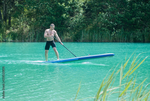 A man with a paddle on a Board is sup surfing on a lake with turquoise water