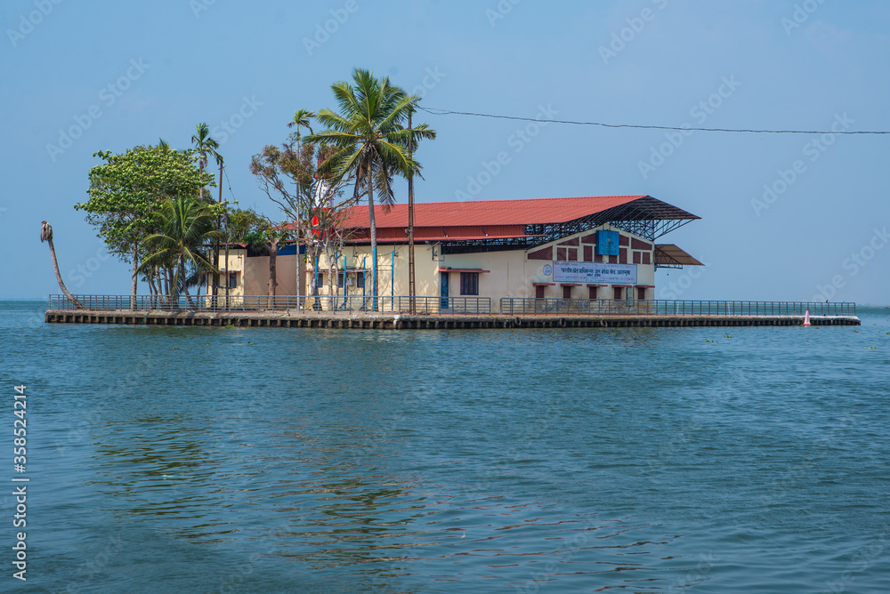 Small houses in a local village located next to Kerala's backwater on a bright sunny day and traditional Houseboat seen sailing through the picturesque backwaters of Allapuzza or Alleppey in Kerala 