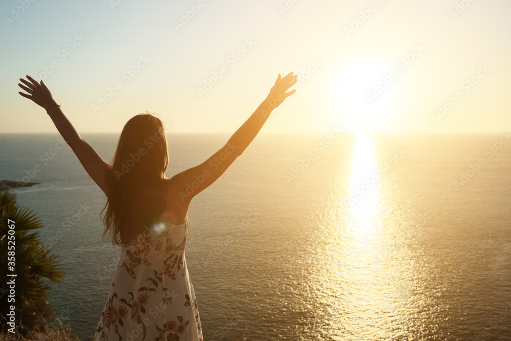 female silhouette raises hands and admires pictorial sunset standing on beach edge at sunset