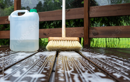 Brush and plastic canister with detergent on a wooden board, wooden terrace. Technologies and tools for cleaning surfaces.
