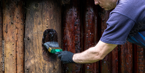 Treatment of wood logs, protective soil, oil on wood. A Caucasian man, paints a log wall of a country house.