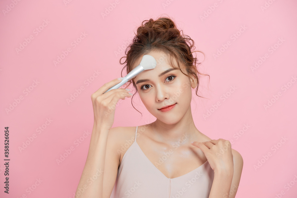 Gorgeous young beautiful Asian woman applying makeup isolated over pink background. Gorgeous young beautiful Asian woman applying makeup isolated over pink background.