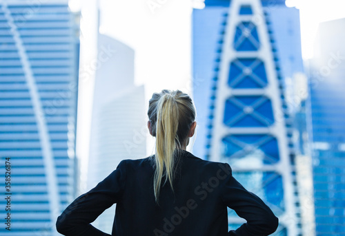 Business career challenge. Ambitious businesswoman overlooking the city center high-rise buildings with hands on hips. Back view.