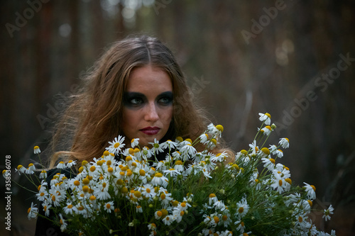 witch girl with a bouquet of daisies in a dark pine forest © makam1969