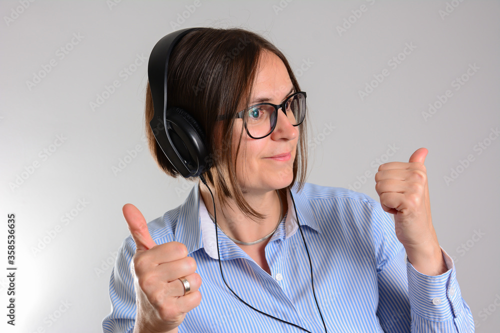 Portrait of satisfied woman enjoying melody via earphones. She is moving and looking down. Isolated on grey background. Portrait of satisfied woman enjoying melody via earphones. She is moving and looking down. Isolated on grey background.