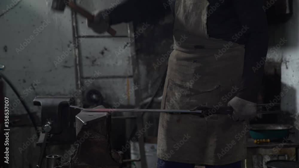Blacksmith Hitting a Hot Red Piece of Metal with a Hummer. Man Forging Hot Iron in a Workshop. The Process of Making Blades for Knifes and Steel Arms Blacksmith Hitting a Hot Red Piece of Metal with a Hummer. Man Forging Hot Iron in a Workshop. The Process of Making Blades for Knifes and Steel Arms