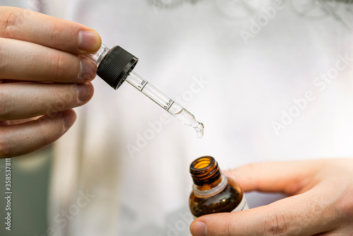 The person holds the bottle in his hand and takes a dose of the medicine with a dropper