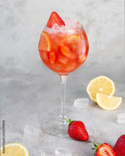Refreshing strawberry lemonade with lemon slices in a glass steamed glass on a gray background. Advertising a drink for the catalog. Lemon halves, strawberries and ice. Food styling of a summer drink.