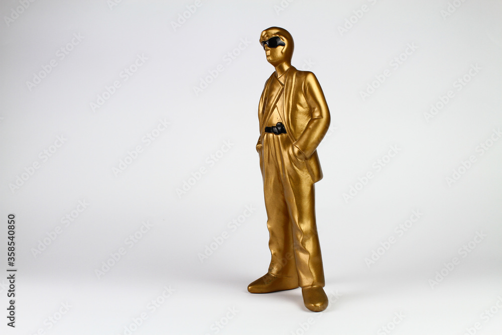 Golden plaster man figure in classic suit, sunglasses and hands in pockets. White background. Golden plaster man figure in classic suit, sunglasses and hands in pockets. White background.