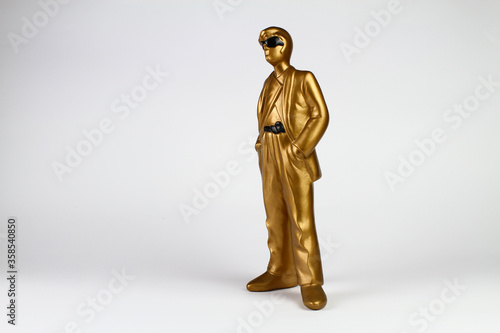 Golden plaster man figure in classic suit, sunglasses and hands in pockets. White background.