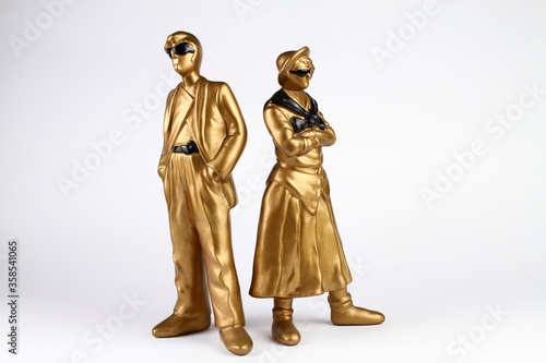 Golden plaster figures of man and woman. Vintage style. The man in a classic suit and sunglasses, the woman in a skirt and shirt with sunglasses and folded arms. White background