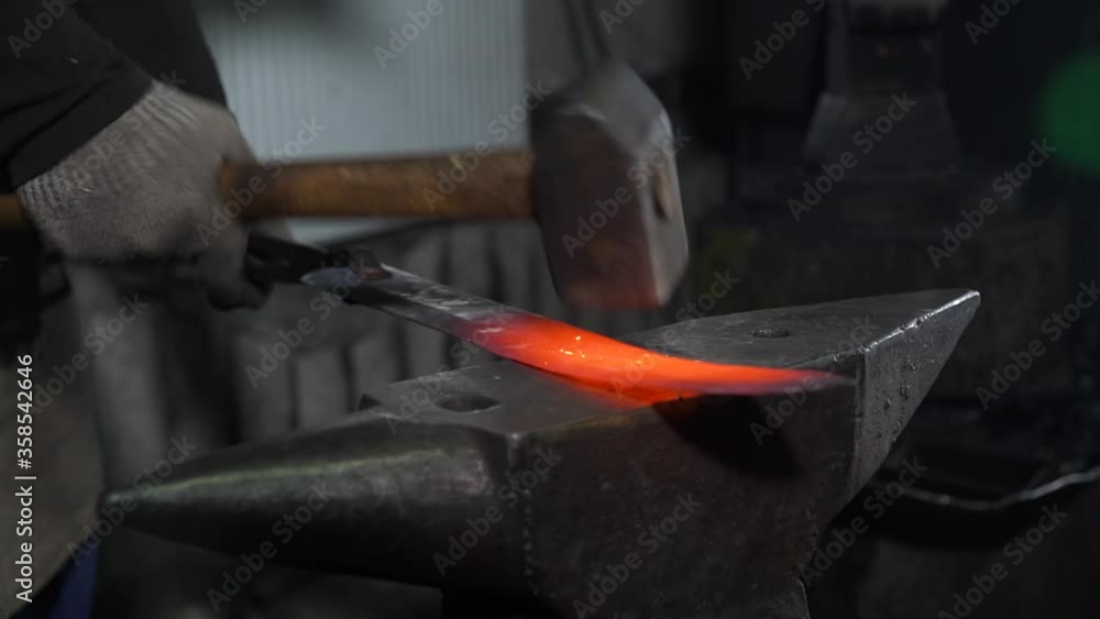 Blacksmith Forging Sword Blade in Smithy. Closeup of Man Hitting the Hot Red Metal with a Hummer on the Anvil. The Process of Making Blades for Knifes and Steel Arms Blacksmith Forging Sword Blade in Smithy. Closeup of Man Hitting the Hot Red Metal with a Hummer on the Anvil. The Process of Making Blades for Knifes and Steel Arms