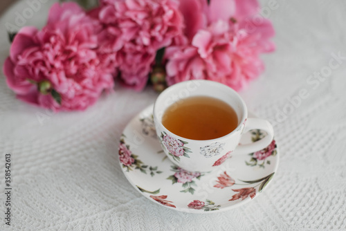 pink peonies on the table with a cup of tea