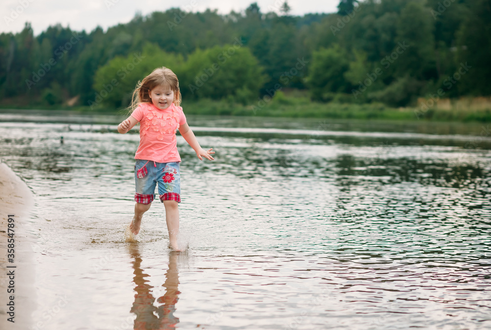 Little happy girl runs along the river and splashes water on a sunny summer day. Laughs. Copy space Little happy girl runs along the river and splashes water on a sunny summer day. Laughs. Copy space