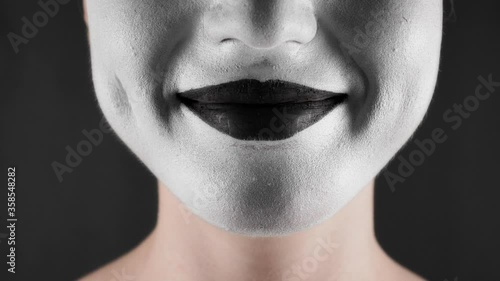 Portrait of a mime and bodypainting woman in white with black lips. Woman's lips on black background close-up