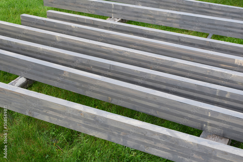 Natural wooden planks laying on green field grass just painted in  brown grey color outdoors.
