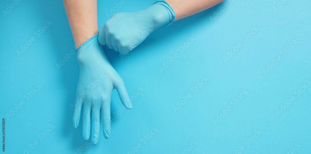 The hand is pulling doctor gloves or blue latex gloves of the right hand on blue background. The hand is pulling doctor gloves or blue latex gloves of the right hand on blue background.