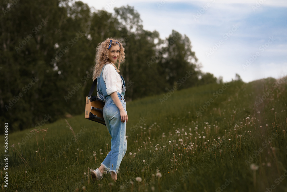 Fototapeta premium girl with curly hair and in denim overalls goes uphill on green grass