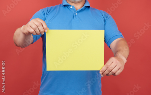 man in blue clothes holds an empty sheet of yellow paper on a red background