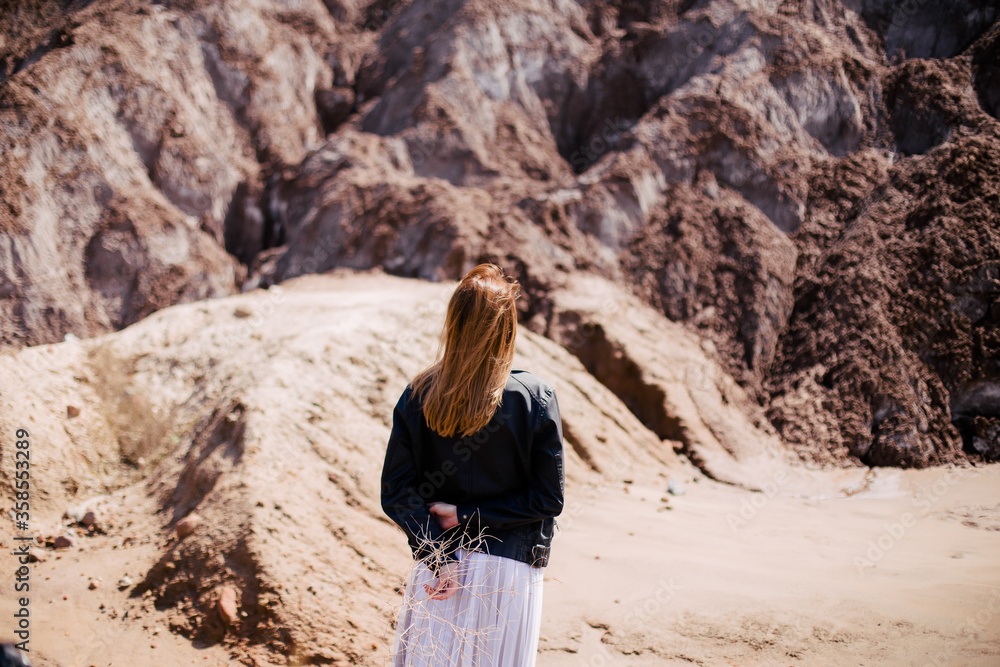 Naklejka premium A young girl in a dress and a leather jacket stands in the mountains