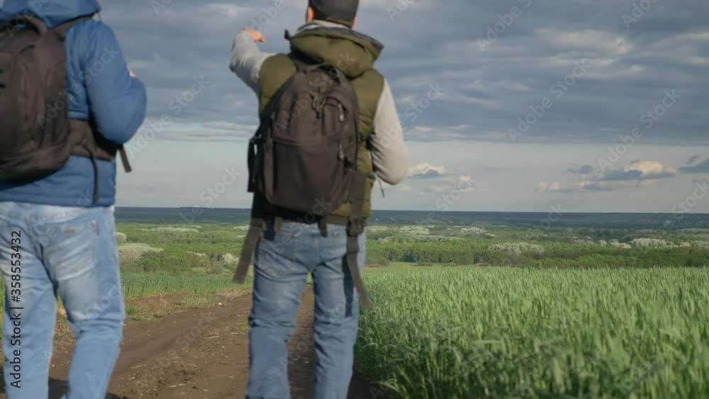 teamwork travel. two man hikers with backpacks walk along a trail next to a field with green grass in nature. concept adventure travel hiking healthy lifestyle. two tourists walk lifestyle walking teamwork travel. two man hikers with backpacks walk along a trail next to a field with green grass in nature. concept adventure travel hiking healthy lifestyle. two tourists walk lifestyle walking