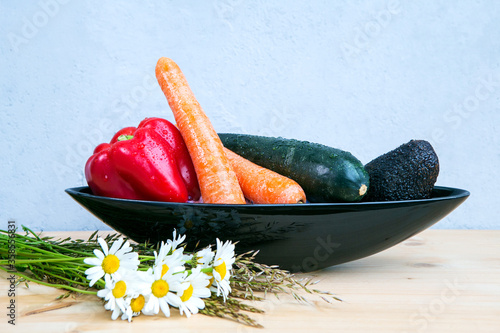 avocado, bell pepper, carrots and cougette in black bowl on wooden table with daisies photo