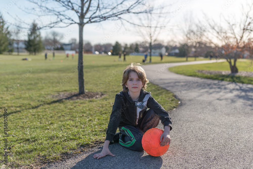 Fototapeta premiumPortrait of a child sitting on the ground and holding a bright orange soccer ball