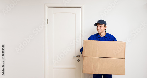 Young happy delivery man in blue uniform is shipping a parcel for the client. © Med Photo Studio