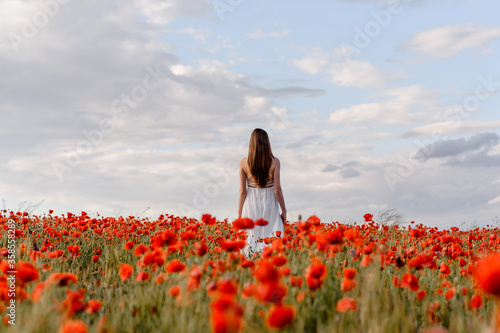 Back view of a woman in white dress walking in a red poppies field