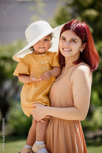Portrait of a young happy beautiful mother with her little smiling daughter wearing a funny oversize white hat and looking at the camera