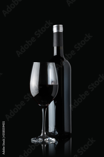 Glass of red wine next to a bottle isolated on black background