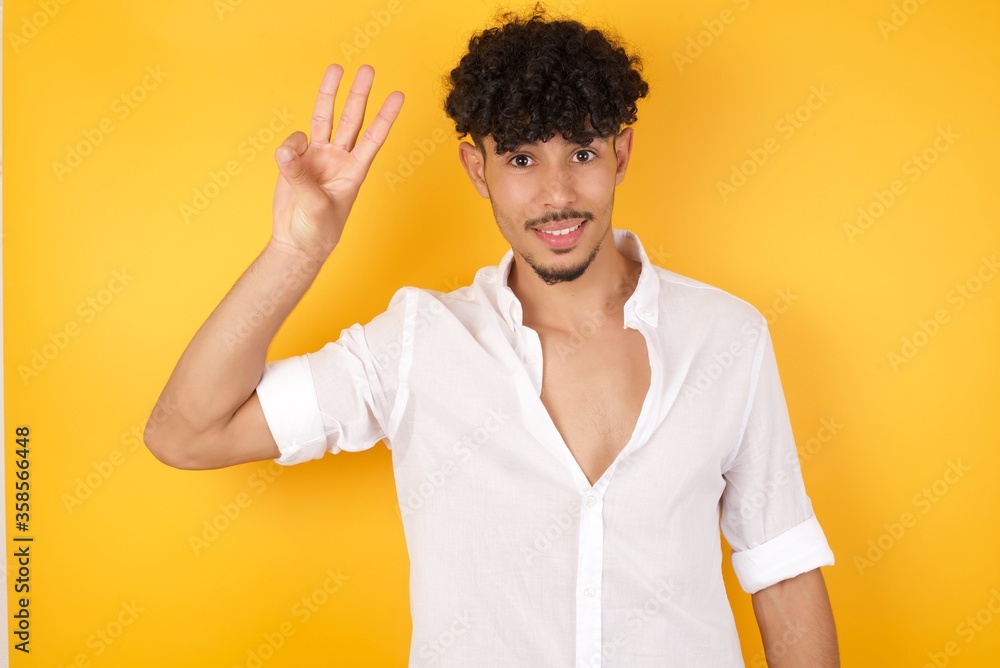 Young blond man standing standing against gray wall showing and pointing up with fingers number three while smiling confident and happy. Young blond man standing standing against gray wall showing and pointing up with fingers number three while smiling confident and happy.