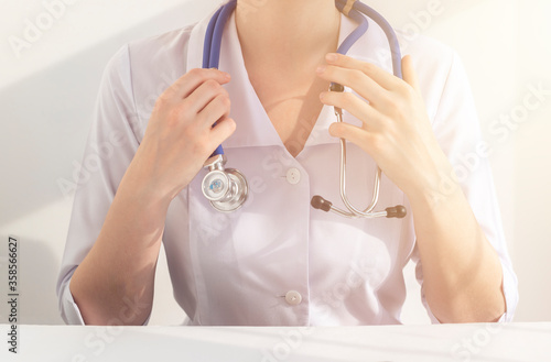 female doctor at the table with stethoscope on her neck taking stethoscope with hands. docotor in hospital at workplace photo