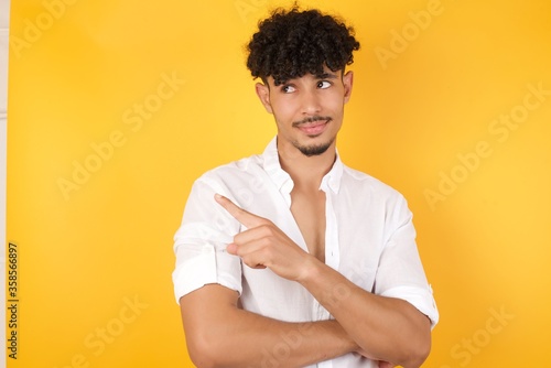 Portrait of young man posing on camera with tricky look and gesturing to side. Male designer presenting lovely product with index finger. Gesture concept.