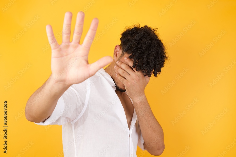 People, body language. Young European man covers eyes with palm and doing stop gesture, tries to hide from everybody. Don't look at me, I don't want to see, feels ashamed or scared. People, body language. Young European man covers eyes with palm and doing stop gesture, tries to hide from everybody. Don't look at me, I don't want to see, feels ashamed or scared.