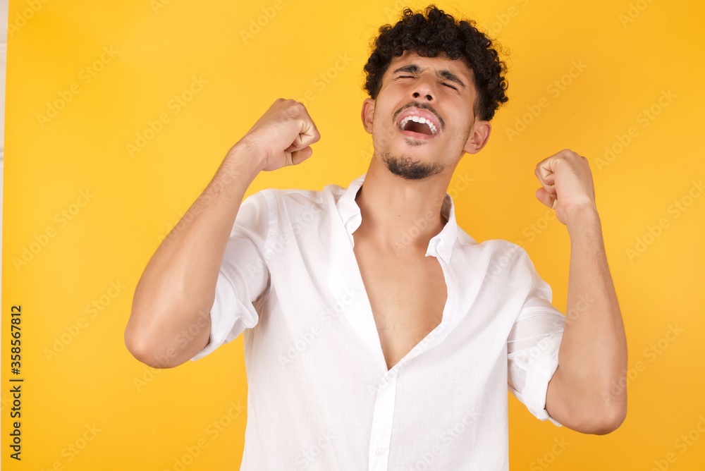 Portrait of handsome male looks with excitement up, keeps hands raised, notices something unexpected, poses indoors. Lovely man reacts on sudden news. Portrait of handsome male looks with excitement up, keeps hands raised, notices something unexpected, poses indoors. Lovely man reacts on sudden news.