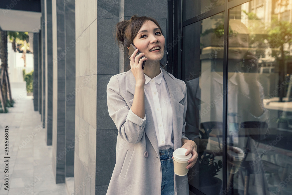 Asian women talking with mobile phones and holding coffee cub go to work on the streets in the morning. Asian women talking with mobile phones and holding coffee cub go to work on the streets in the morning.