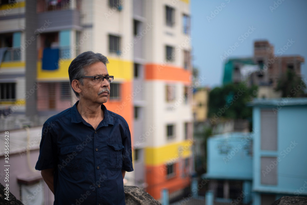 Body portrait of an An old/aged Indian Bengali man in blue shirt is standing on a rooftop under the open sky in front of a urban landscape. Indian lifestyle and seniors Body portrait of an An old/aged Indian Bengali man in blue shirt is standing on a rooftop under the open sky in front of a urban landscape. Indian lifestyle and seniors