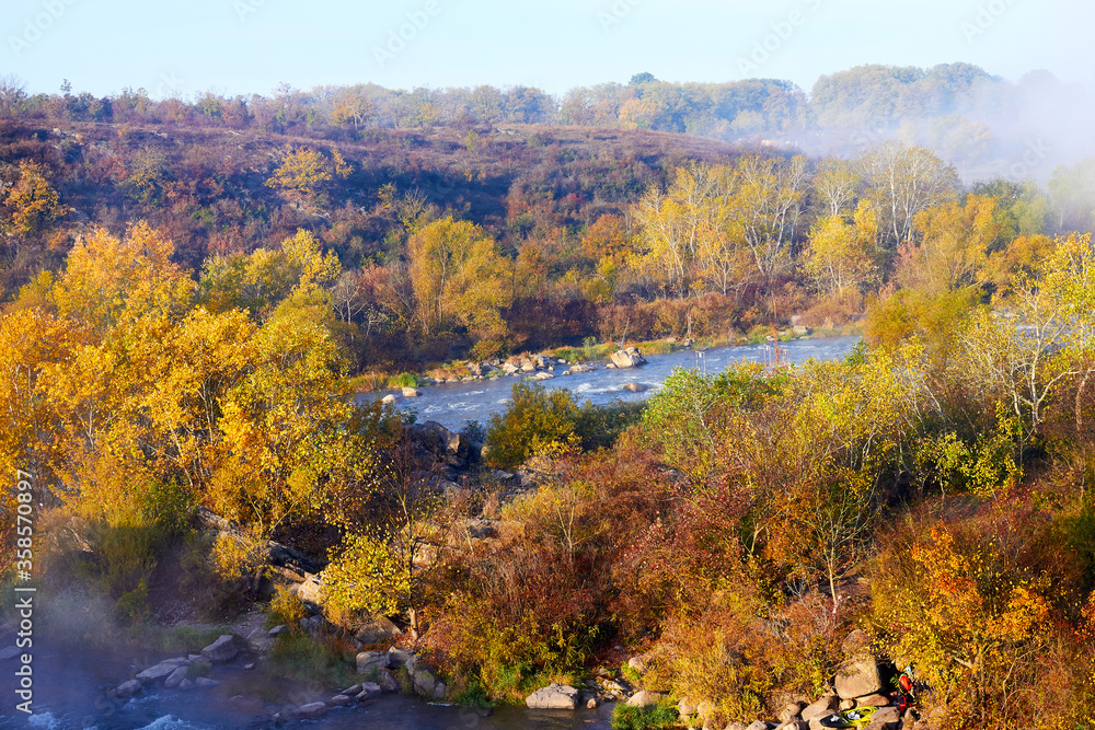 View from above on the river with the rapids in a light haze and crowns of autumn trees