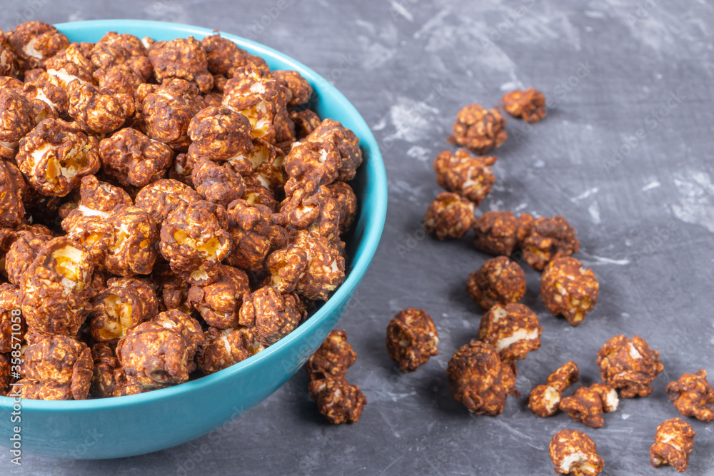 Chocolate popcorn in a blue cup on a dark background. Sprinkled popcorn is next to the cup. Chocolate popcorn in a blue cup on a dark background. Sprinkled popcorn is next to the cup.
