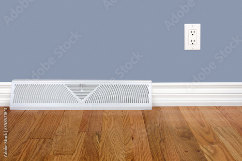 Bedroom wall with heating register, baseboard, electrical outlet and hardwood floor.