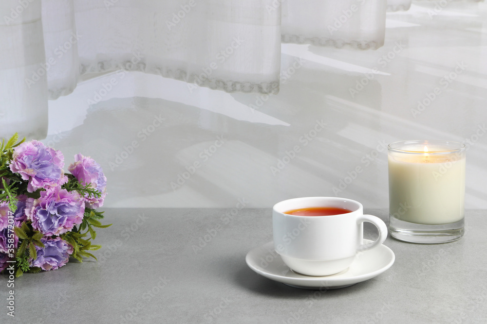 a white cup of red tea and a glass of candle are on the grey table with bouquet of flowers in the white living room near the white curtain a white cup of red tea and a glass of candle are on the grey table with bouquet of flowers in the white living room near the white curtain