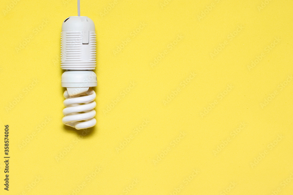 Energy saving lamp hanging from the ceiling, yellow background. Electricity conservation concept, place for text, copy space. The photo Energy saving lamp hanging from the ceiling, yellow background. Electricity conservation concept, place for text, copy space. The photo