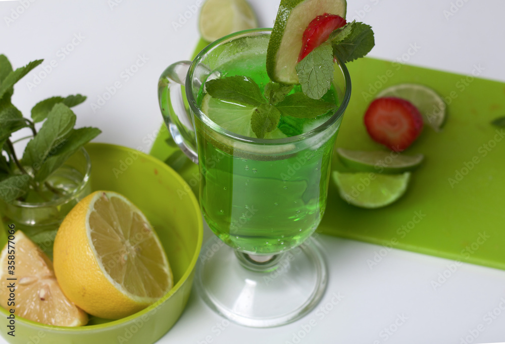 Green lemonade in a glass. Decorated with lime and strawberries. With sprigs of mint. Near lemon and mint. Green lemonade in a glass. Decorated with lime and strawberries. With sprigs of mint. Near lemon and mint.