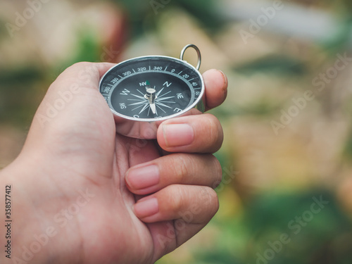 Hand of child hand using magnetic golden compass while traveling in the jungle or forest and looking for an adventure route to mountain or hill. Epic landscape concept.