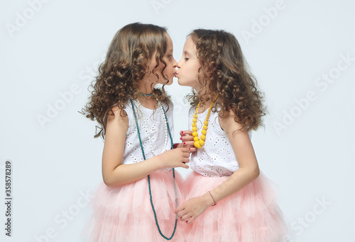 two little girls play with their mother's high-heeled shoes. they pose and try to be adults.Studio, White background